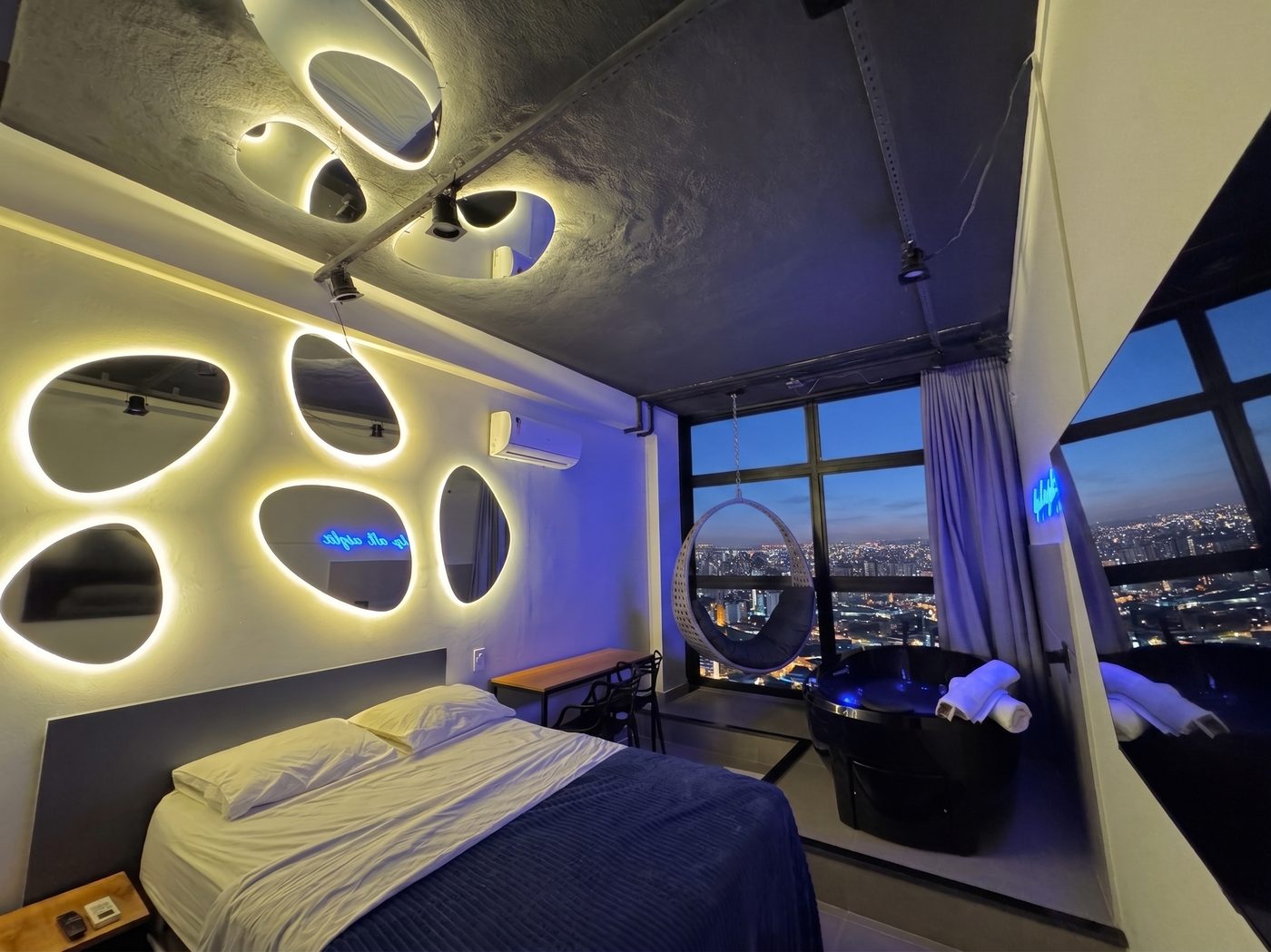 Suíte Reflection Room com parede de espelhos e cadeira suspensa, vista de São Paulo